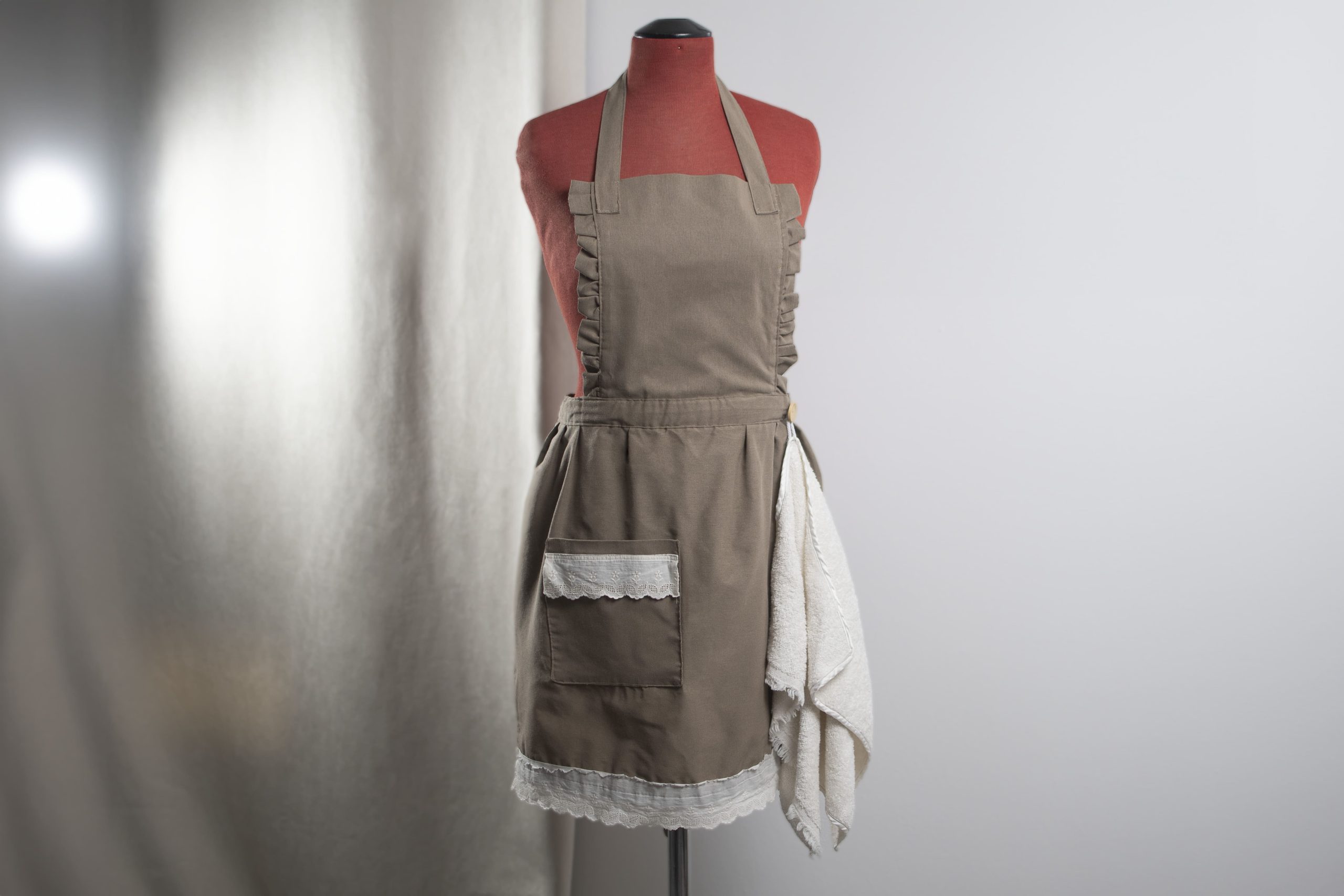 Grembiule artigianale in tessuto grigio con tasca e bordo in pizzo bianco su manichino