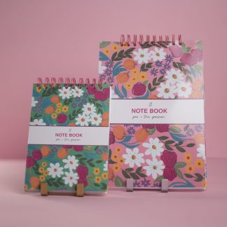 Due notebook a spirale con copertine floreali colorate, uno verde e uno rosa, su sfondo rosa