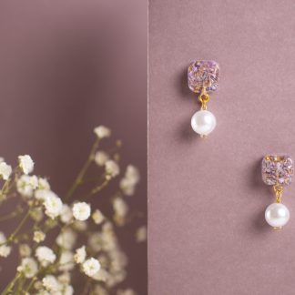 Orecchini artigianali con perla bianca pendente e base quadrata floreale viola su fondo rosa