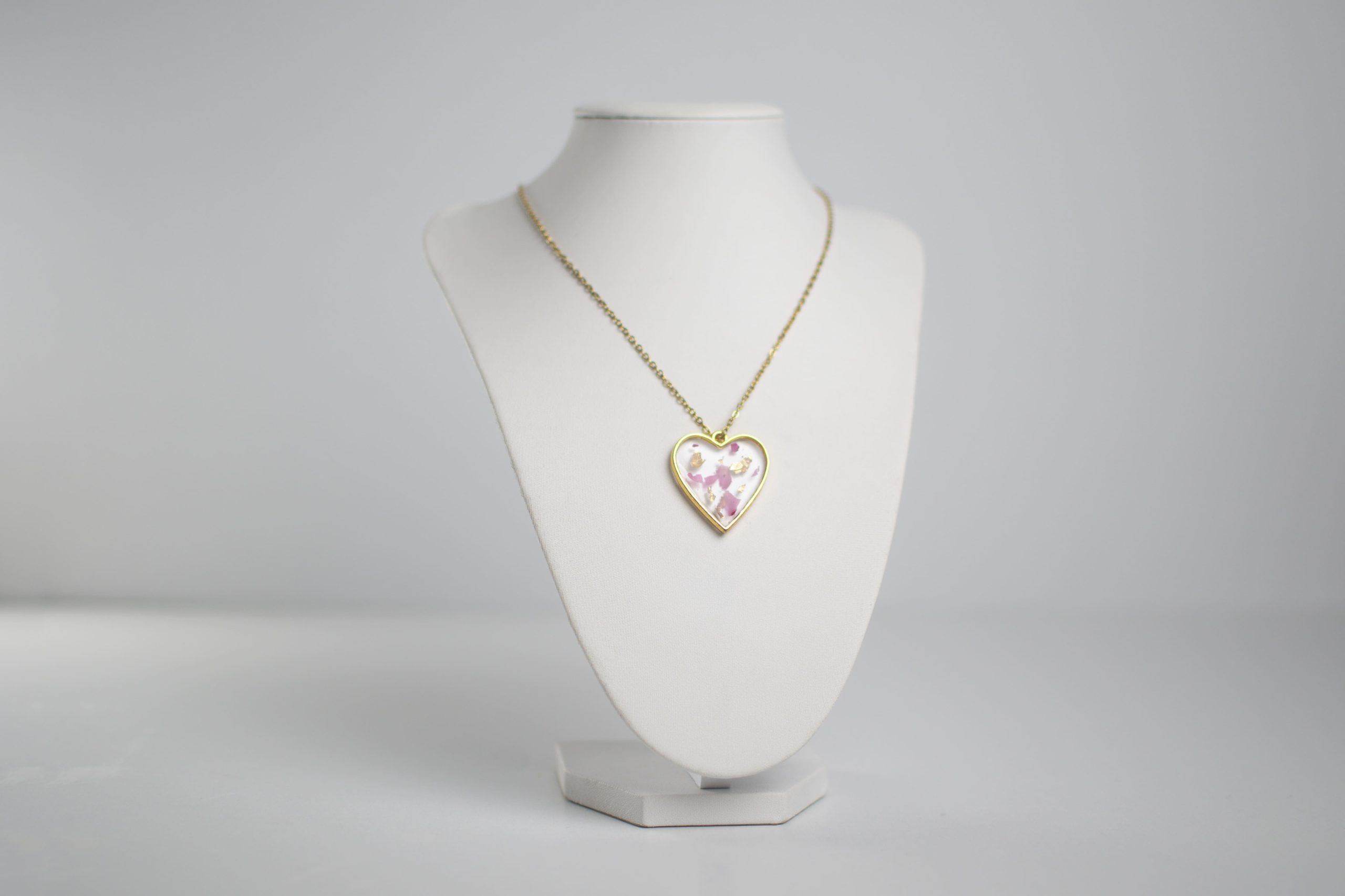 Collana a cuore con inserto bianco, rosa e oro su catena dorata esposta su supporto bianco
