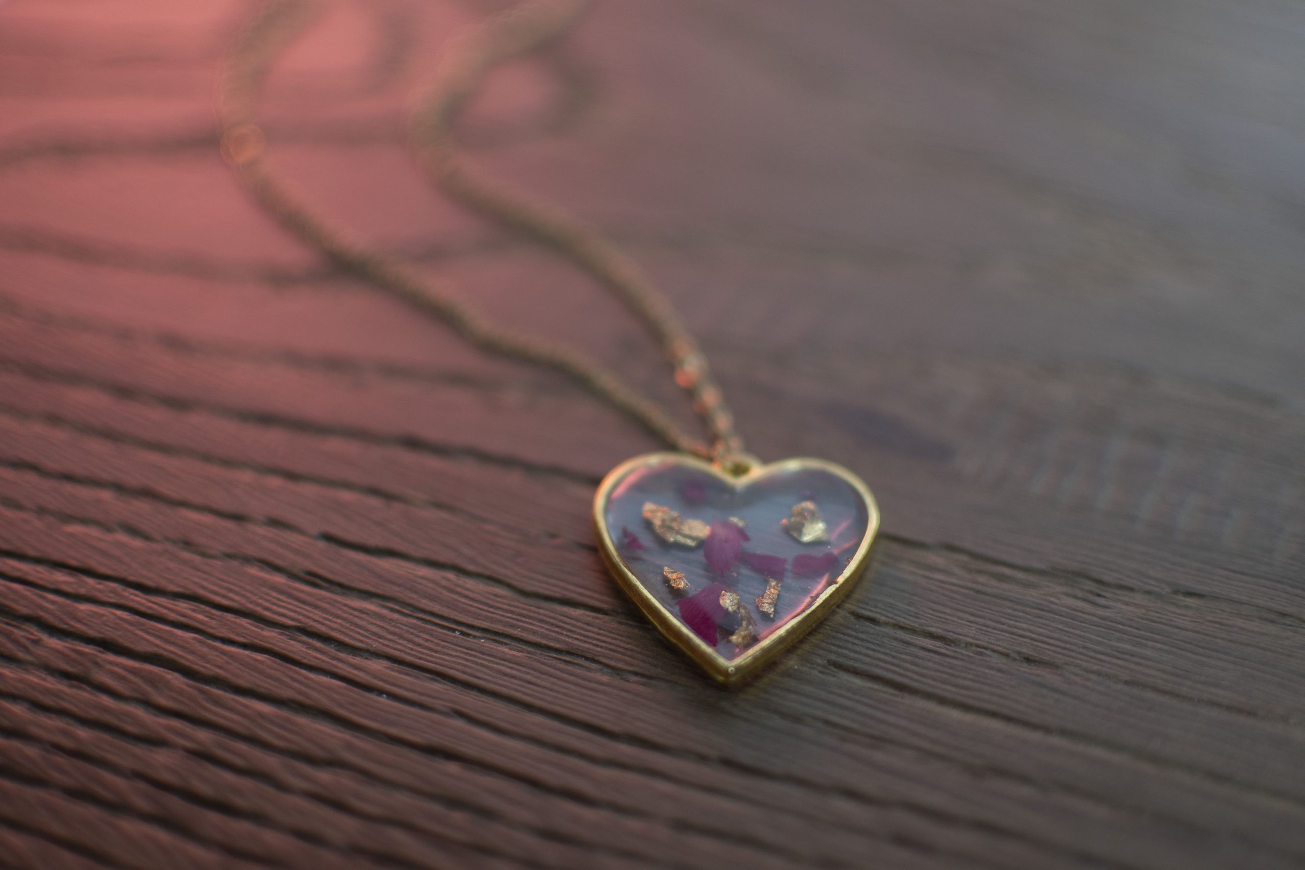 Collana con ciondolo a cuore trasparente con inserti rosa e foglia oro appoggiata su fondo in legno