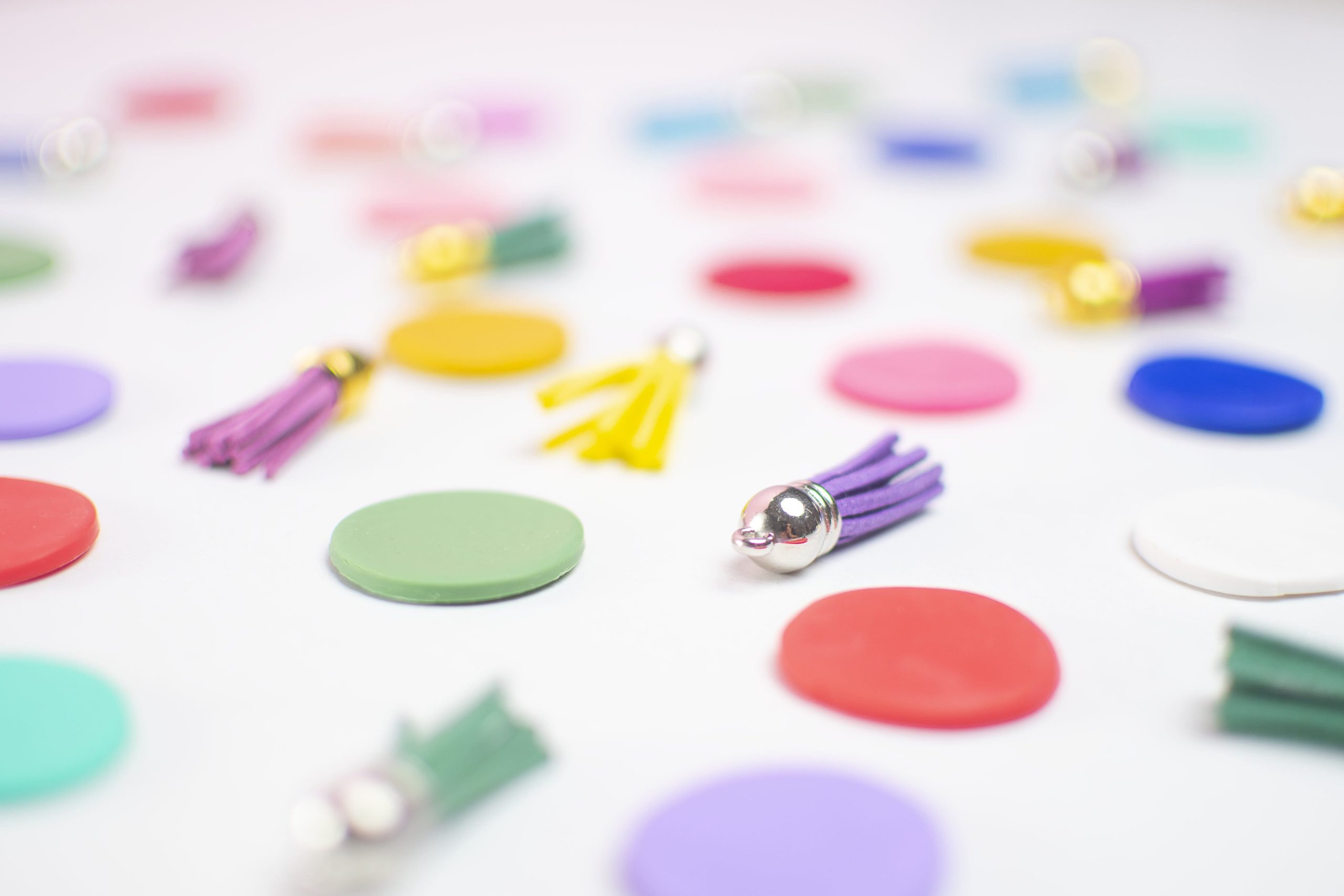Decorazioni artigianali con nappine in pelle colorata e dischetti multicolore su sfondo bianco